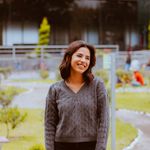 A cheerful woman wearing a gray sweater smiling casually in a park setting in Puebla, Mexico.